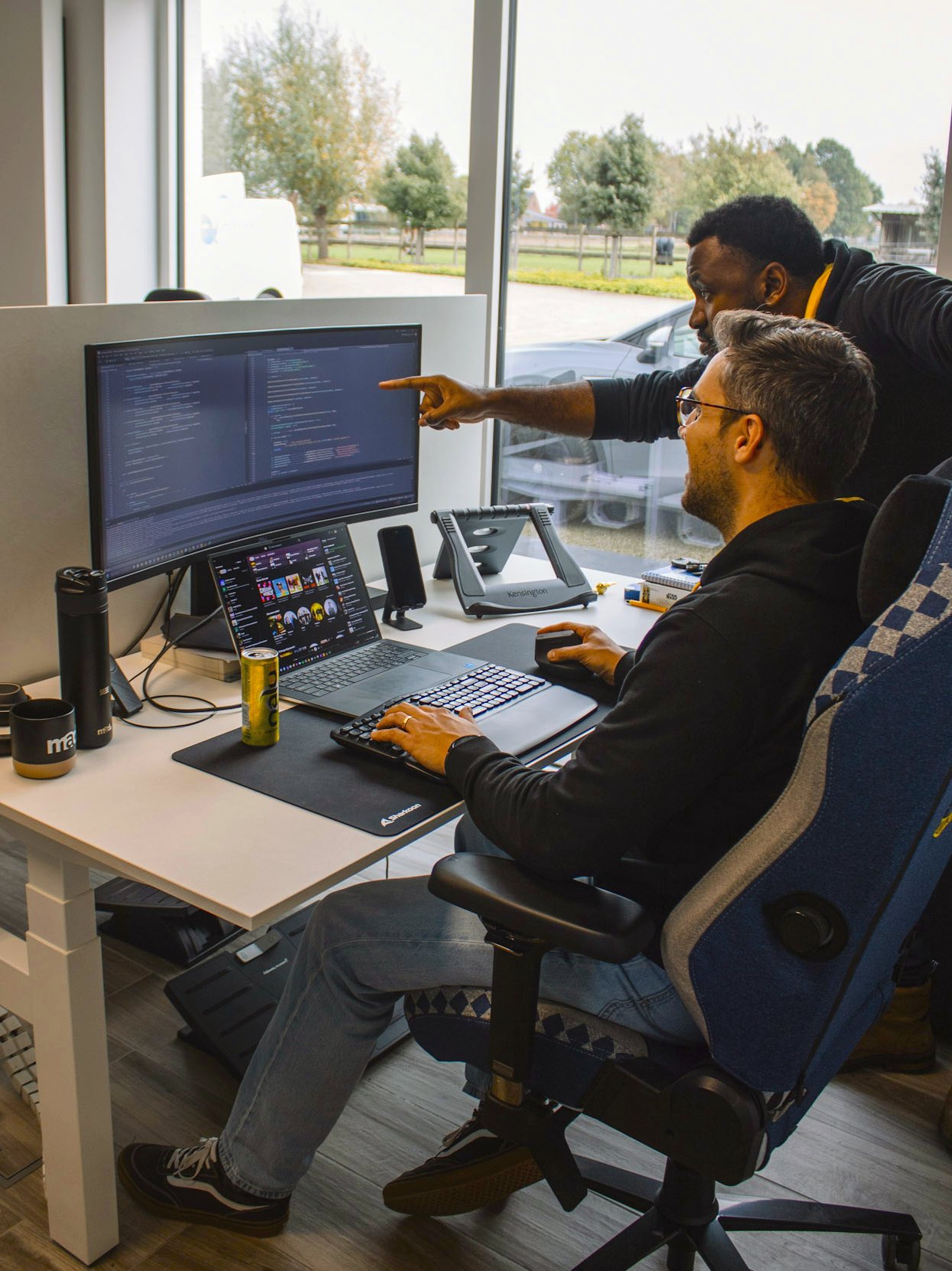 Twee IT-specialisten van Mad IT werken samen aan softwareontwikkeling op een modern kantoor, met meerdere schermen en code op het beeldscherm – focus op samenwerking, maatwerk software en digitale transformatie.